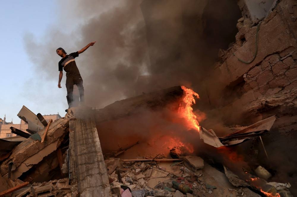 A Palestinian man gestures as he stands on the rubble of a collapsed building as a fire burns following a strike by the Israeli military on Khan Yunis in the southern Gaza Strip Saturday. AFP