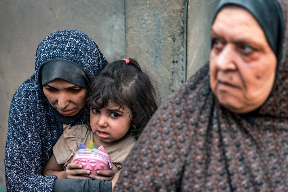 A Palestinian family sits near destroyed houses following a strike in Rafah on the southern Gaza Strip on Monday. AFP