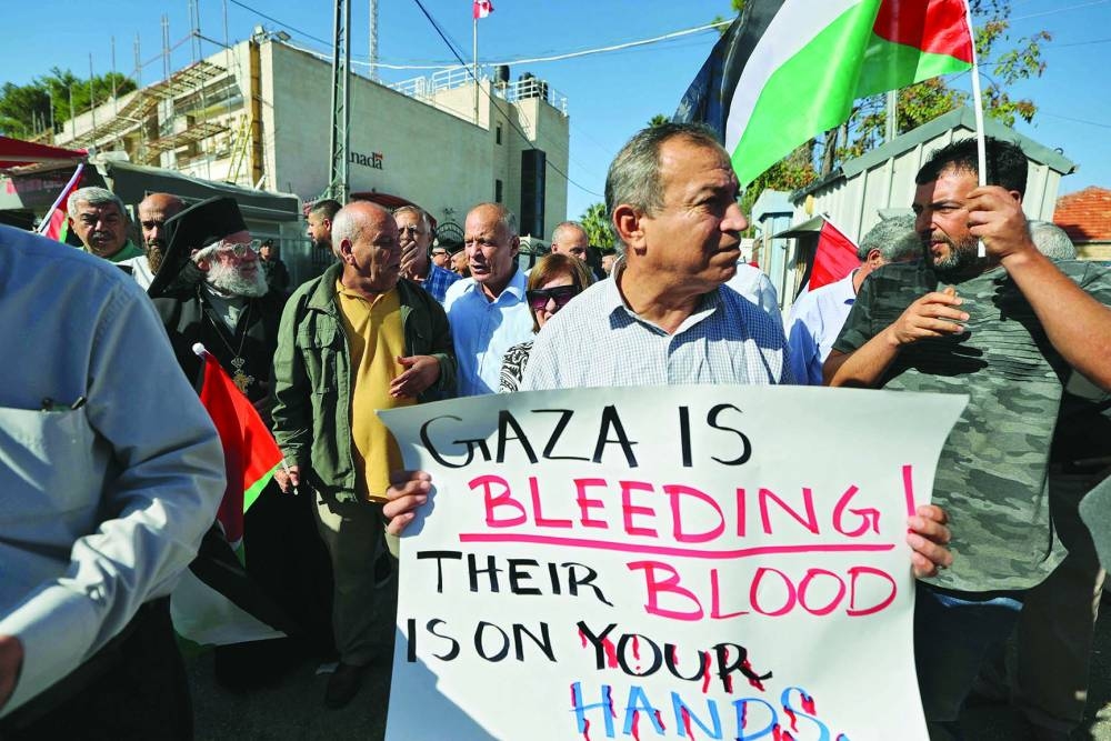 
Palestinians hold placards and wave national flags during a protest in solidarity with Gaza outside the Canadian consulate in the West Bank city of Ramallah, yesterday. 