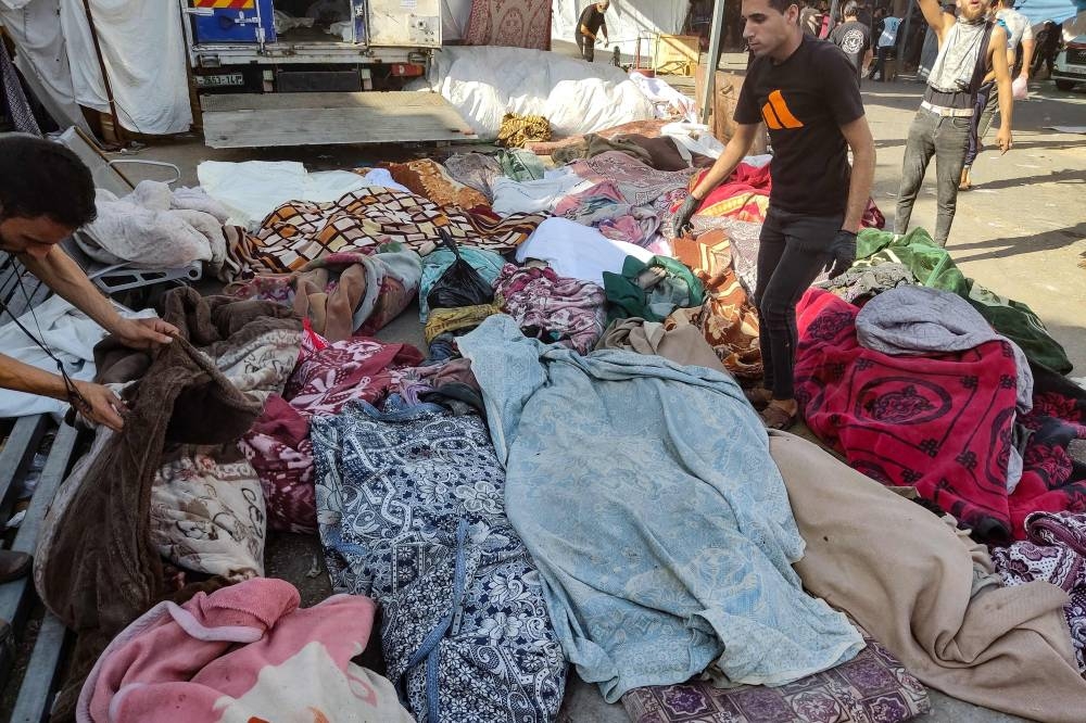 Men check the bodies of people killed in bombardment that hit a school housing displaced Palestinians, as they lie on the ground in the yard of Al-Shifa hospital in Gaza City, on Friday. AFP