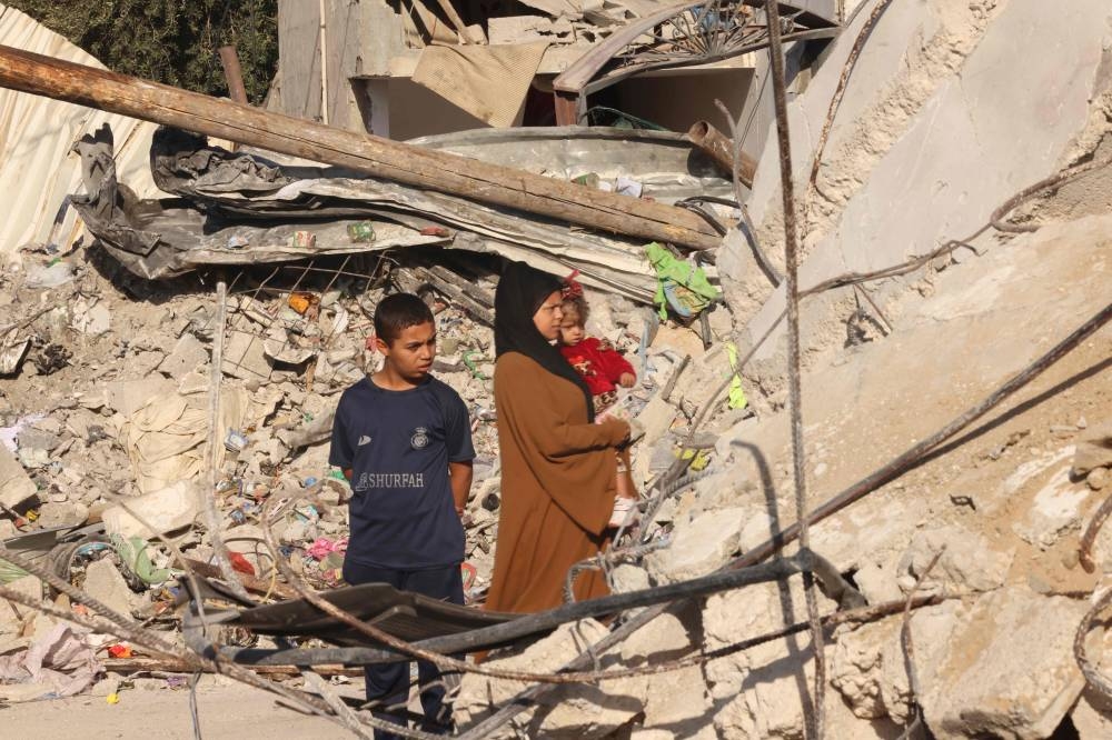 A Palestinian woman holds a child as she stands amongst the rubble of collapsed buildings destroyed in the Israeli bombardment of Rafah in the southern Gaza Strip, on Friday. AFP