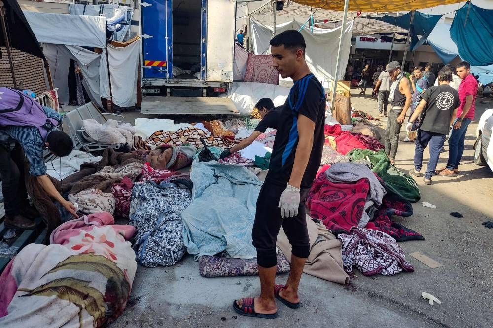 Men check the bodies of people killed in bombardment that hit a school housing displaced Palestinians, as they lie on the ground in the yard of Al-Shifa hospital in Gaza City on Friday. AFP