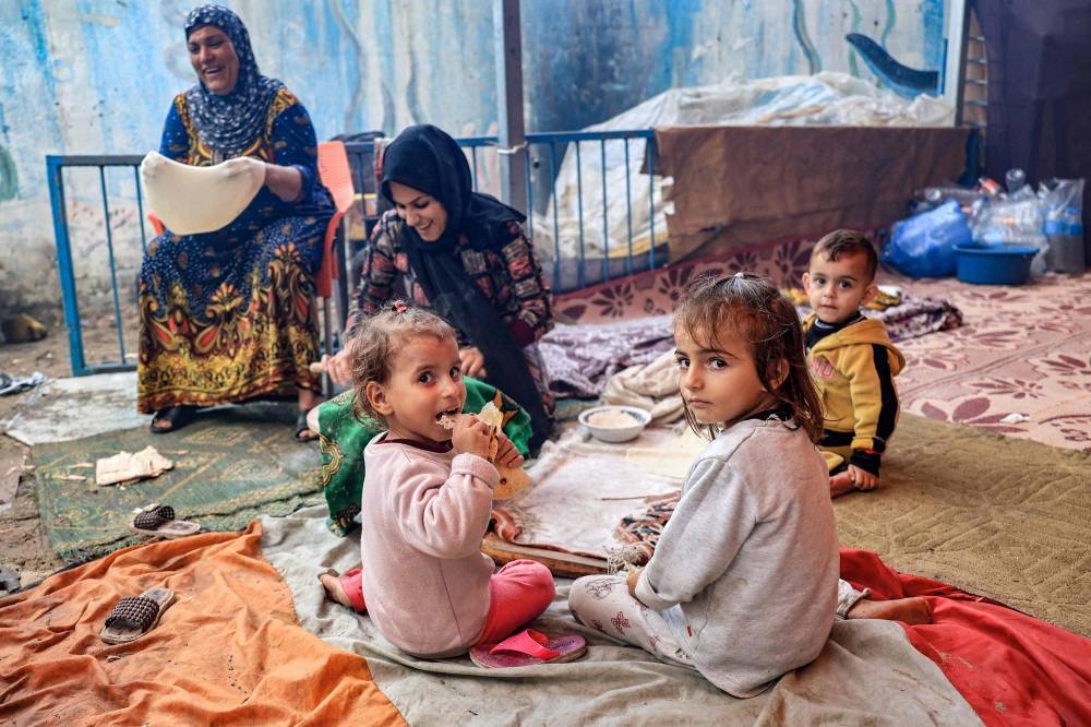 Children sit by a woman preparing traditional unleavened bread on an open fire at school run by the United Nations Relief and Works Agency for Palestine Refugees in the Near East (UNRWA) in Rafah in the southern Gaza Strip, on Tuesday. AFP