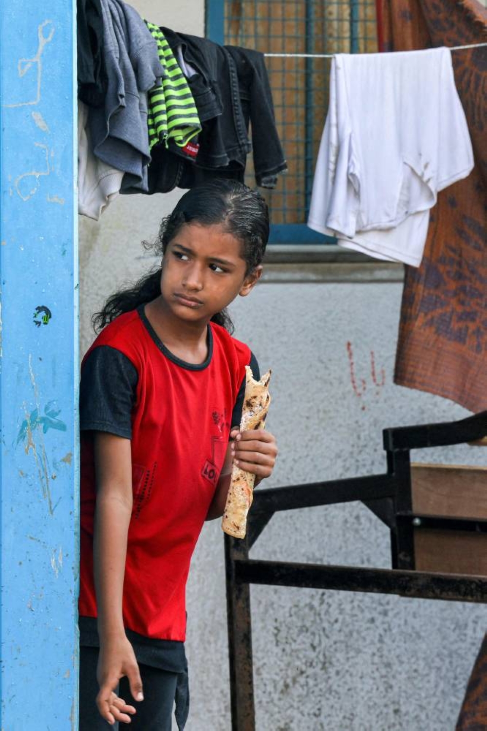A girl holds a sandwich wrap as she stands behind laundry drying on a line at a school run by the United Nations Relief and Works Agency for Palestine Refugees in the Near East (UNRWA) in Rafah in the southern Gaza, on Tuesday. AFP
