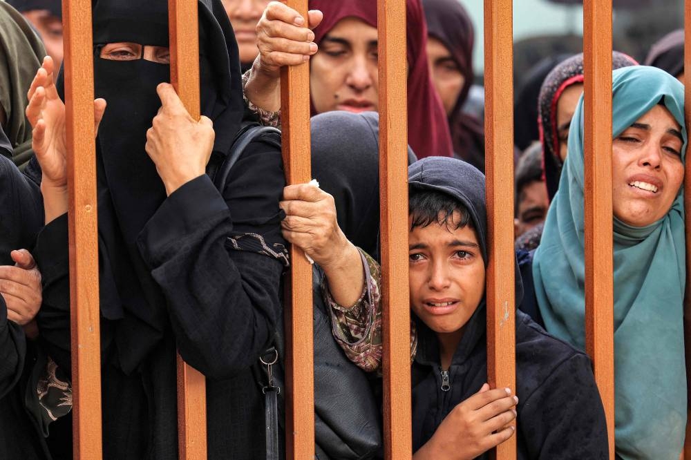 People mourn as they stand behind a metal fence near the bodies of victims who were killed in Israeli bombardment before their burial, outside the morgue at Nasser hospital in Khan Yunis in the southern Gaza Strip, on Tuesday. AFP