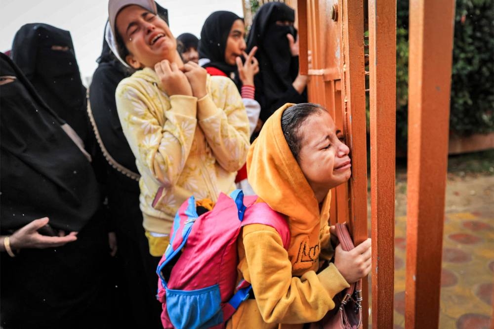 People mourn as they stand behind a metal fence near the bodies of victims who were killed in Israeli bombardment before their burial, at Nasser hospital in Khan Yunis in the southern Gaza Strip, on Tuesday. AFP
