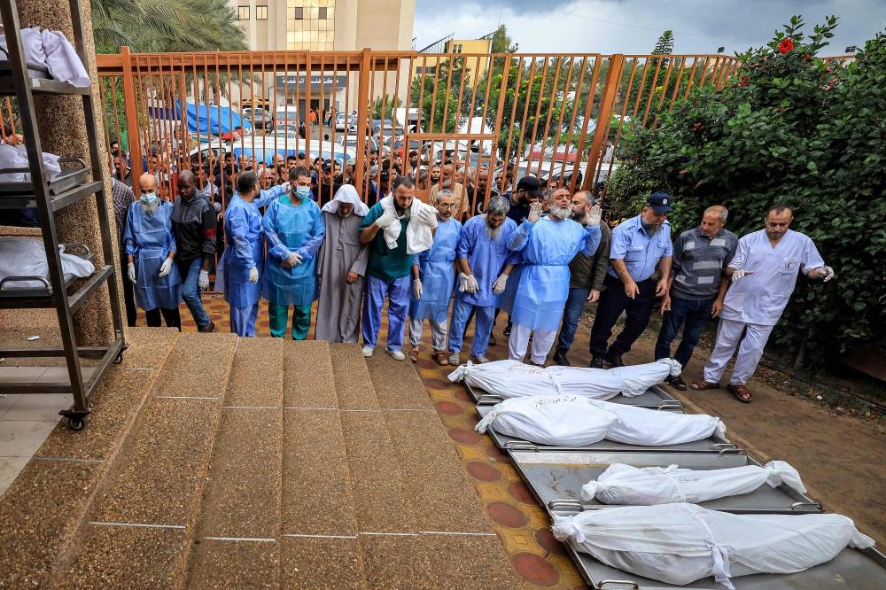 A policeman, physicians, and other men prepare to pray before some of the bodies of victims who were killed in Israeli bombardment before their burial, outside the morgue at Nasser hospital in Khan Yunis in the southern Gaza Strip, on Tuesday. AFP