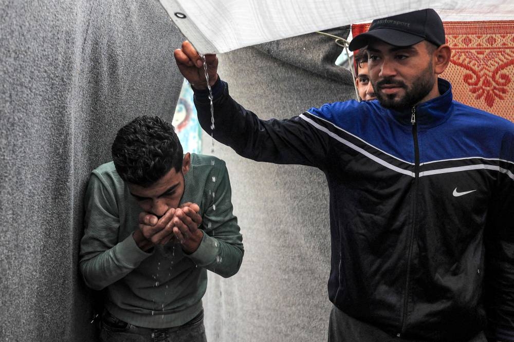 Men use their hands to drink rainwater dripping from the roof of a tent amid water shortages while at a school run by the United Nations Relief and Works Agency for Palestine Refugees in the Near East (UNRWA) in Rafah in the southern Gaza Strip on Tuesday. AFP