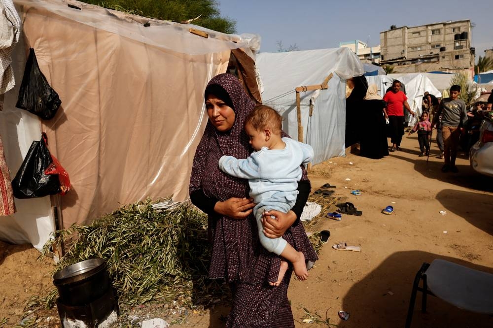 A woman walks while carrying a child as displaced Palestinians, who fled their houses due to Israeli strikes, shelter in tents at Nasser hospital in Khan Younis in the southern Gaza Strip, on Sunday. REUTERS