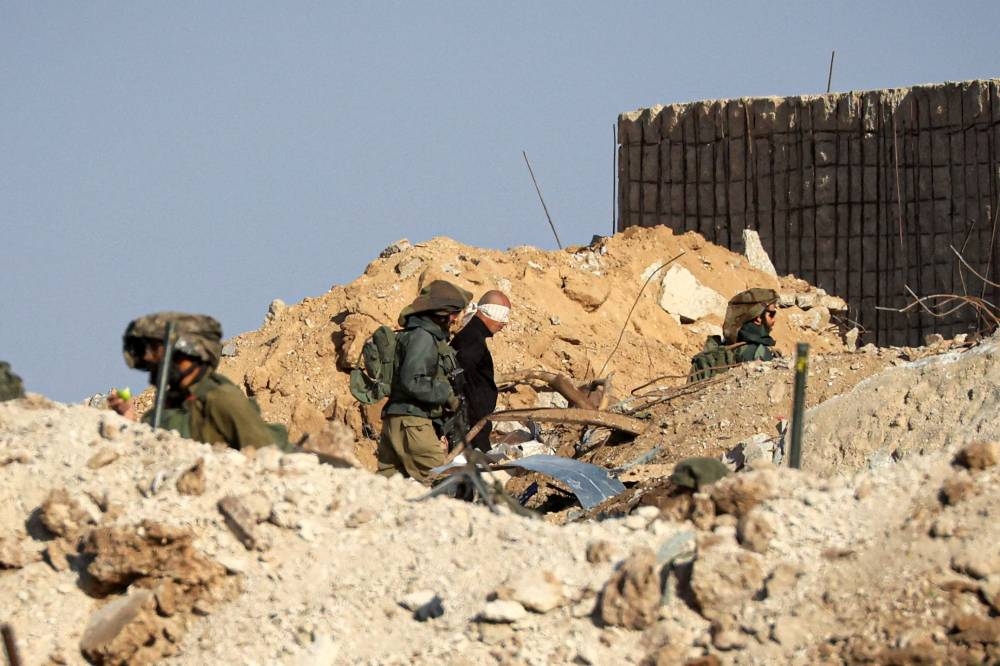 Israeli soldiers detain blindfolded Palestinian men in a military truck while watching Palestinians (not pictured) fleeing the fighting in war-torn Gaza walk by on a road in the Zeitoun district of the southern part of the Gaza Strip on Monday. AFP
