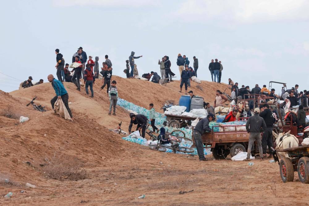 Palestinians pick up drinking water bottles that reportedly ended up on the Palestinian side of the Rafah crossing between Egypt and the southern Gaza Strip following a windy and rainy night, on November 20, 2023, on Monday. AFP