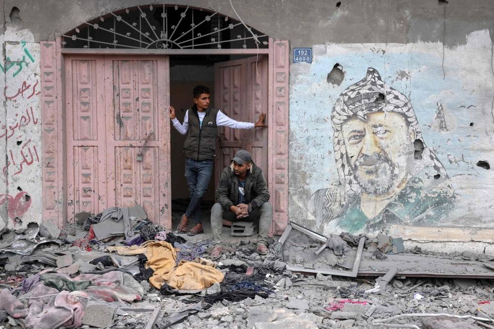 Palestinians stand next to a mural of late Palestinian leader Yasser Arafat amidst the debris following Israeli bombardment on Rafah, in the southern Gaza Strip on Wednesday. AFP