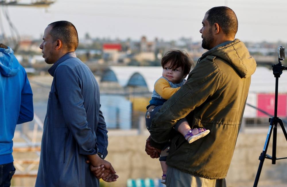 A man holds a child as people gather at Rafah border as Hamas militants are expected to release hostages abducted by Hamas during the October 7 attack on Israel as part of a hostages-prisoners swap deal between Hamas and Israel, as seen from southern Gaza Strip on Friday. REUTERS