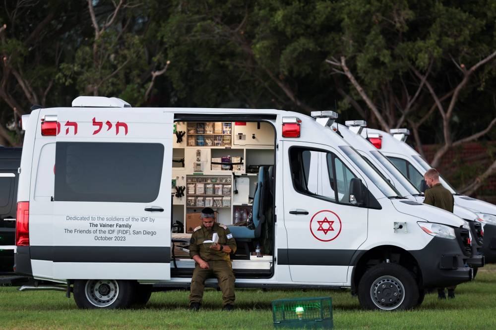 A man reads a book as he sits on an ambulance before the arrival of a vehicle carrying hostages released as part of a deal between Israel and Hamas at Schneider Children's Medical Center in Petah Tikva, Israel, Friday. REUTERS