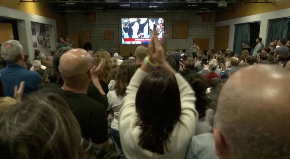 Evacuated residents from Kfar Aza react as they watch on a television the arrival of hostages, in Shefayim, Israel, on Sunday. REUTERS