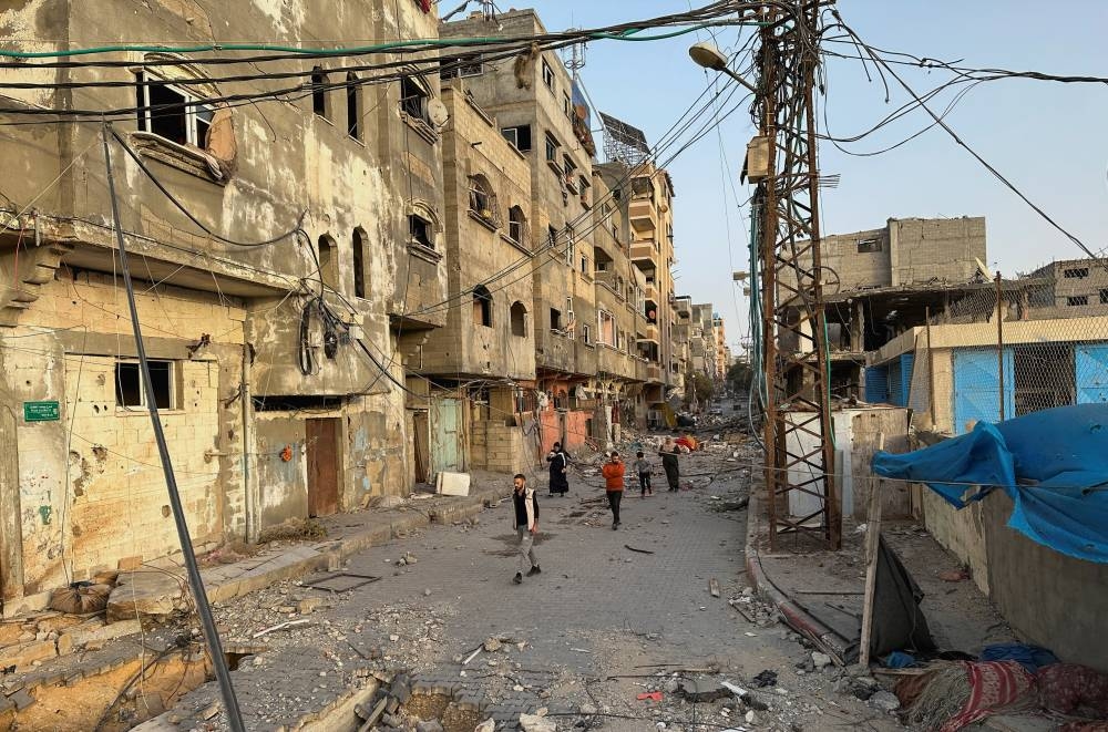 People walk among houses destroyed in Israeli strikes during the conflict, in Beach refugee camp, in Gaza City Sunday. REUTERS