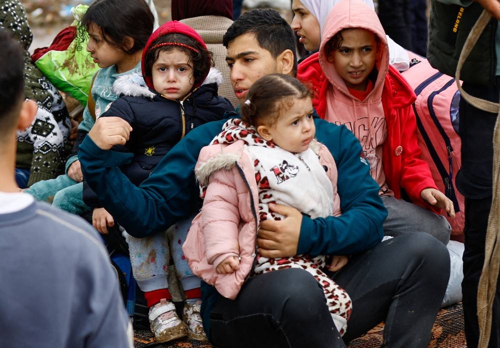 A man sits with children, as Palestinians fleeing north Gaza move southward during a temporary truce between Israel and Hamas, near Gaza City, Monday. REUTERS