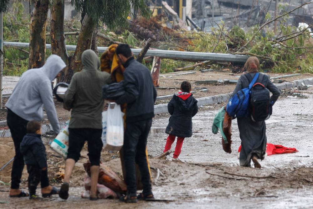 A barefooted Palestinian woman fleeing north Gaza helps her children pick up their belongings as they move southward following rainfall, during a temporary truce between Israel and Hamas, near Gaza City, Monday. REUTERS