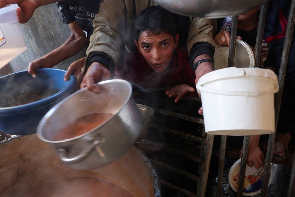 A Palestinian child reacts, while people gather to get their share of charity food offered by volunteers, in Rafah, in the southern Gaza Strip,  Saturday.