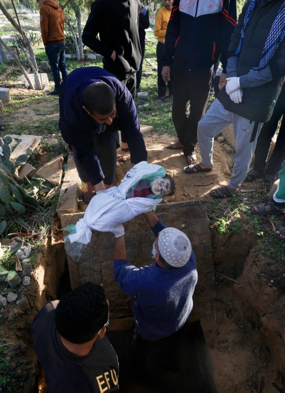 Mourners watch as Palestinian infant Yazan Hams is buried with 12 other members of the same family who were killed in an Israeli air strike on a residential building in Rafah overnight, at a cemetery in the southern Gaza Strip city, early on Monday. AFP