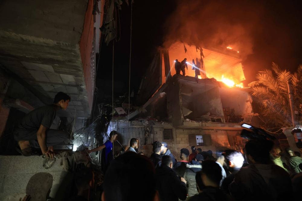 People use the lights on their mobile phones to search for victims amid the rubble of a smouldering building, following an Israeli strike in Rafah in the southern Gaza Strip Wednesday.