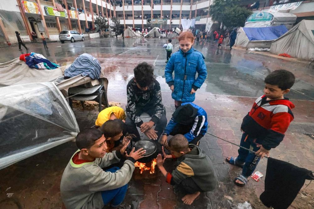 Palestinians children warm up around a fire outside their makeshift tent at a camp set up on a schoolyard in Rafah in the southern Gaza Strip where most civilians have taken refuge, on Wednesday. AFP 
