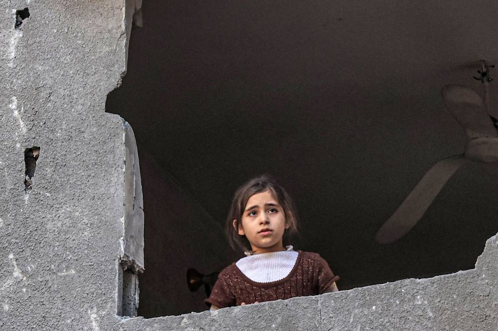 A Palestinian girl looks out the hole of a window of a building damaged by Israeli bombardment in Rafah in the southern Gaza Strip, on Sunday. AFP