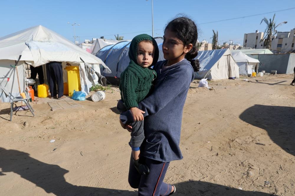 A Palestinian girl carries a child, as displaced Palestinians, who fled their houses due to Israeli strikes, shelter in a tent camp, in Rafah in the southern Gaza Strip, on Sunday. REUTERS