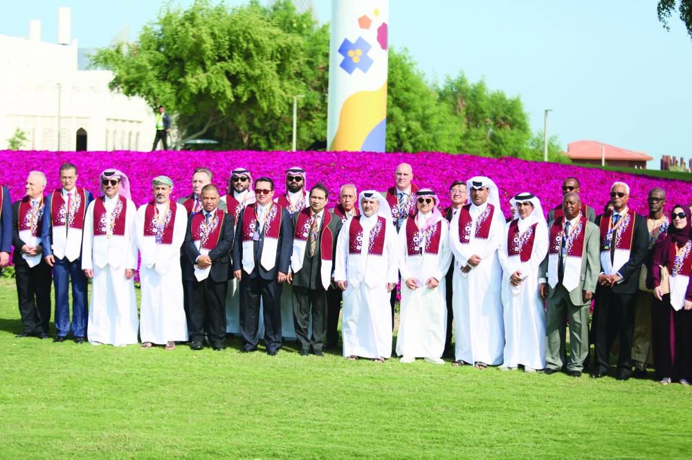 Officials with guests pose near the 'flowery flag' at the Doha Expo 2023 venue