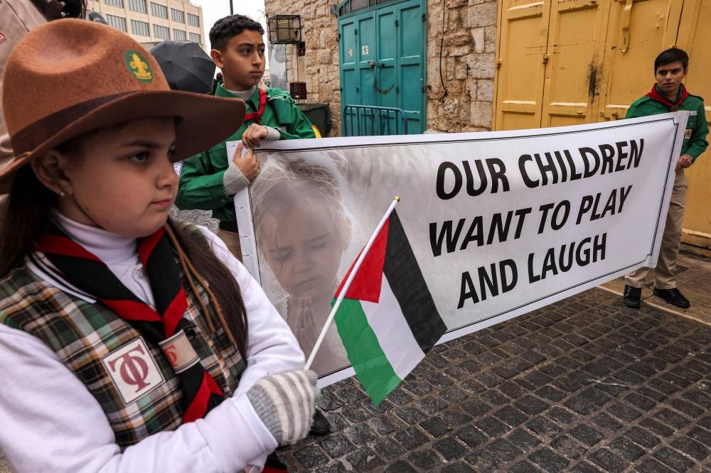 Palestinian youth members of the scouting movement hold up banners condemning and calling for an end of the conflict in the Gaza Strip during a procession welcoming the arrival of the Latin Patriarch of Jerusalem for Christmas Eve celebrations in the biblical city of Bethlehem in the occupied West Bank on Sunday. AFP