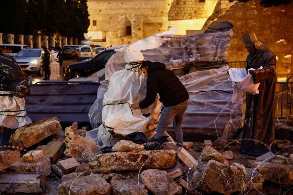 A man unveils a Christmas installation of a grotto with figures standing amid rubble surrounded by a razor wire, outside the Church of the Nativity, in support of Gaza, on Manger Square in Bethlehem, in the Israeli-occupied West Bank, Saturday. REUTERS