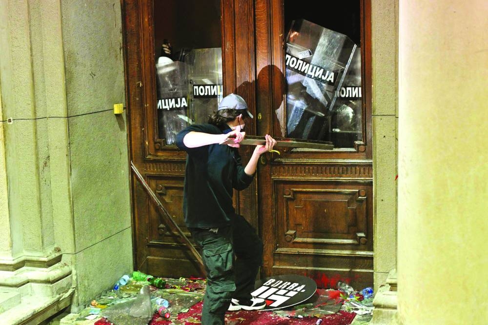
A protester uses a metal object against police officers guarding the entrance to the Belgrade’s city council building during a demonstration in 
Belgrade yesterday. Right: Protestors gathered in front of the same building. (AFP) 