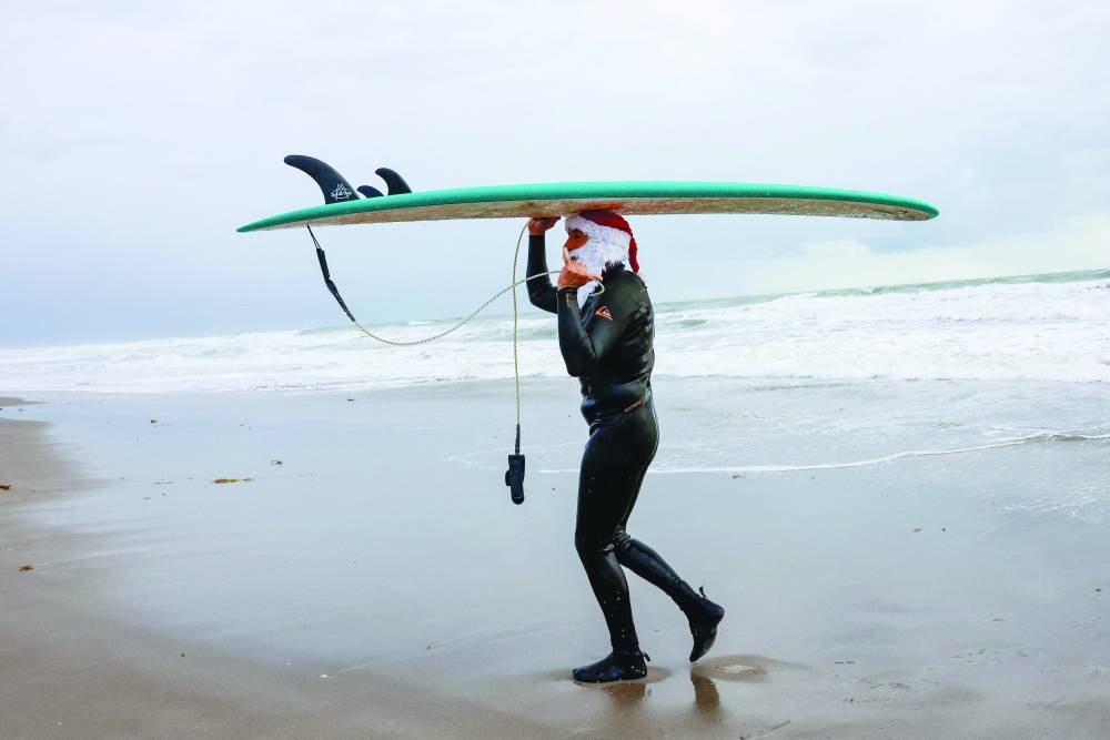 
A surfer dressed as Santa carries a surfboard during the 15th annual “Surfing Santas” event in Cocoa Beach. Right: Surfers dressed as Santa go into the water to ride waves. (AFP) 