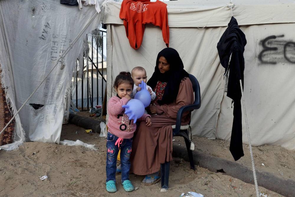 A displaced Palestinian woman sits with children playing with rubber gloves outside a tent in Rafah in the southern Gaza Strip, on Wednesday. AFP