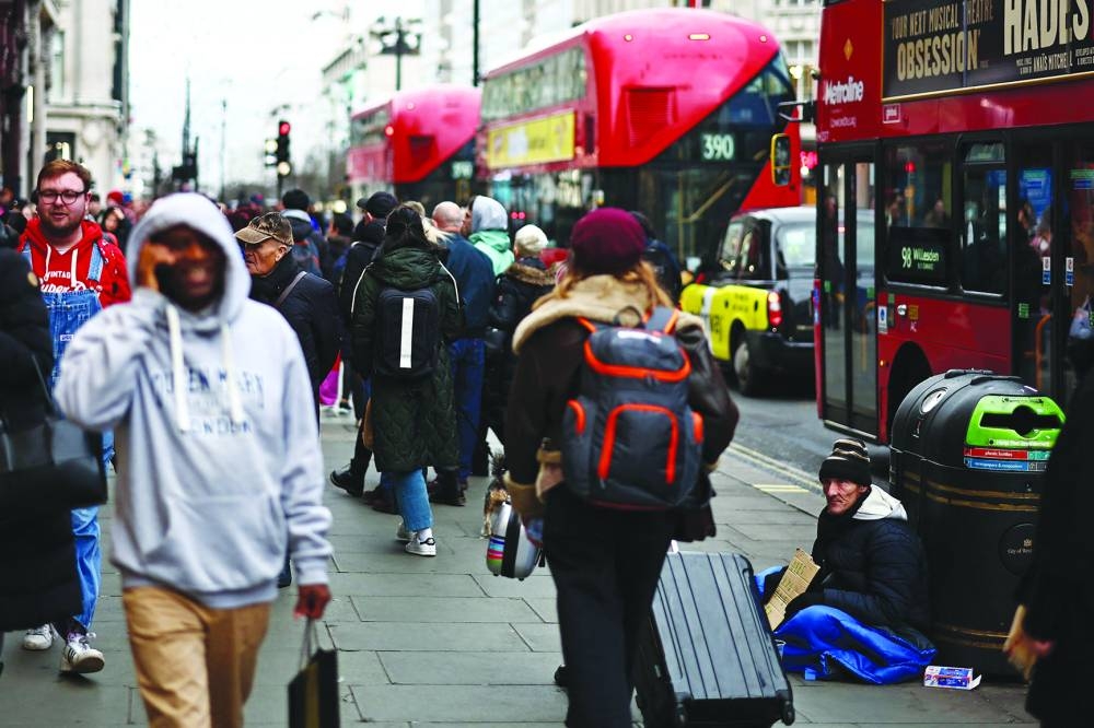 
A beggar sits on the pavement as shoppers and red London buses pass by on Oxford Street in central London. 