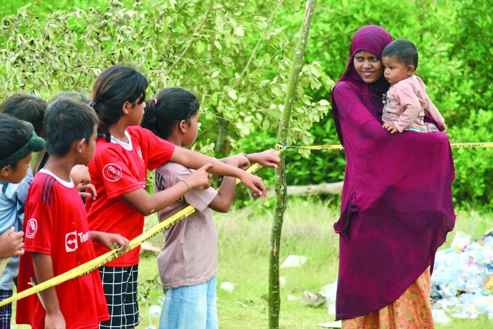 A Rohingya woman carrying her child greets locals at a temporary shelter, following their arrival in Karang Gading village, in Deli Serdang of Indonesia’s Sumatra province.