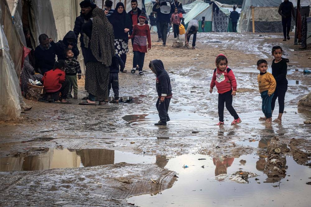 Palestinian children walk in puddles on a muddy path at a makeshift camp housing displaced Palestinians, in Rafah in the southern Gaza Strip on Tuesday. AFP