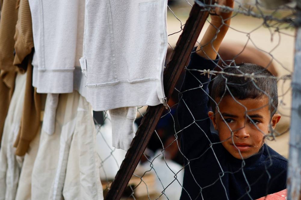 A Palestinian child looks through a fence, as displaced Palestinians, who fled their homes due to Israeli strikes, shelter at a tent camp in Rafah, southern Gaza Strip on Tuesday. REUTERS