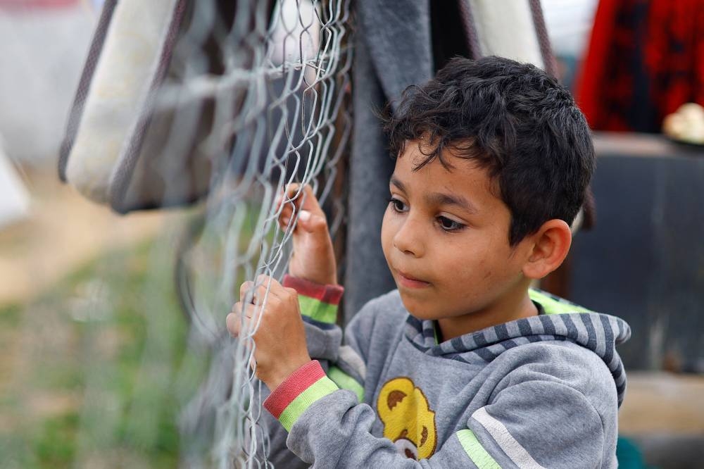 A Palestinian child touches a fence, as displaced Palestinians, who fled their homes due to Israeli strikes, shelter at a tent camp in Rafah, southern Gaza Strip on Tuesday. REUTERS