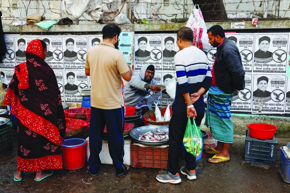 
Posters of an election candidate hang on the wall as a street vendor sells fish, ahead of the general election in Dhaka. 