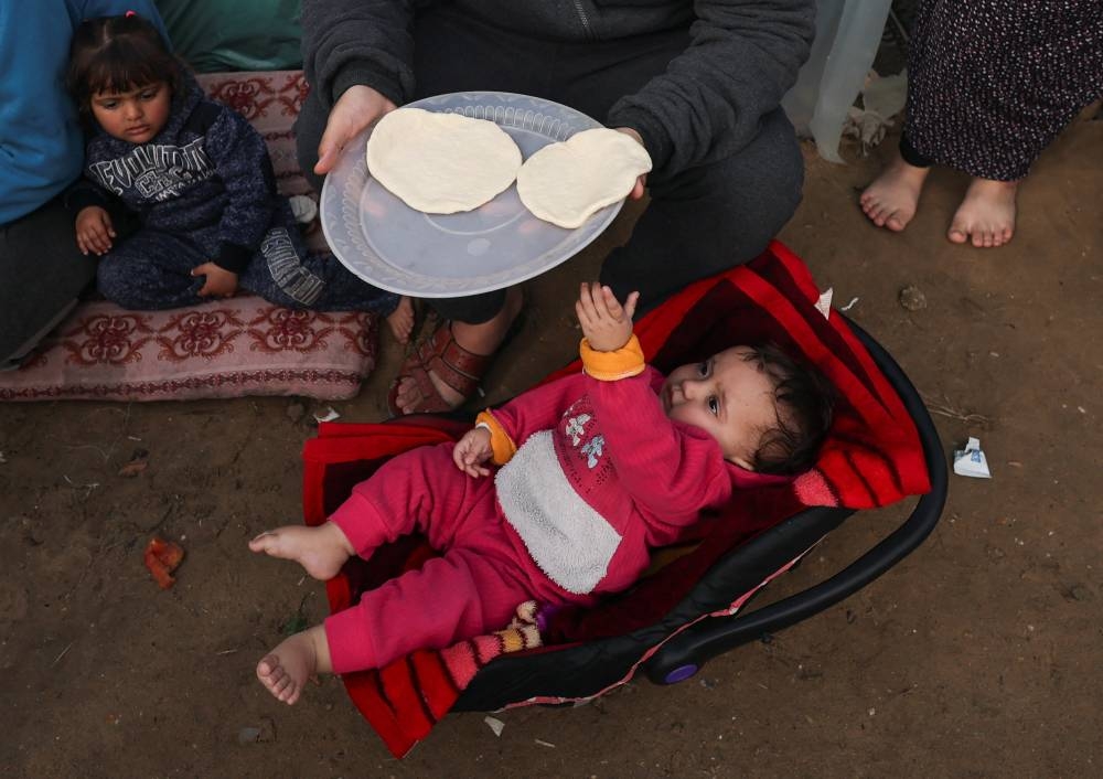A baby reaches for a plate of food as displaced Palestinians, who fled their homes due to Israeli strikes, shelter at a tent camp in Rafah, southern Gaza Strip, on Tuesday. REUTERS