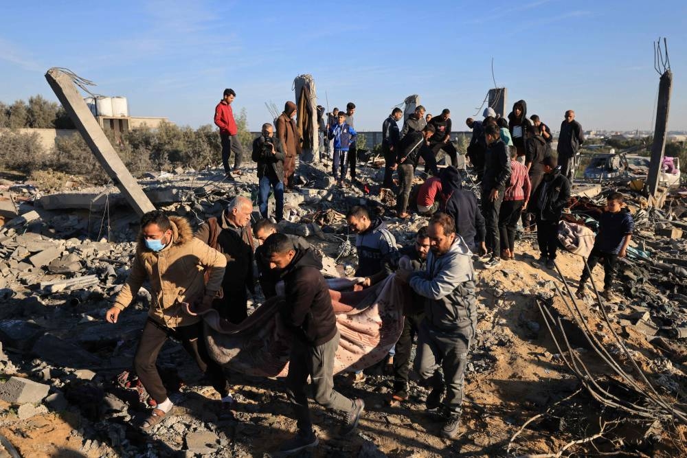 People carry away the body of a victim found under the rubble of a house that was used as a shelter by a displaced Palestinian family, many of whom were reported killed when it was destroyed during an Israeli strike on Rafah in the southern Gaza Strip on Sunday. AFP