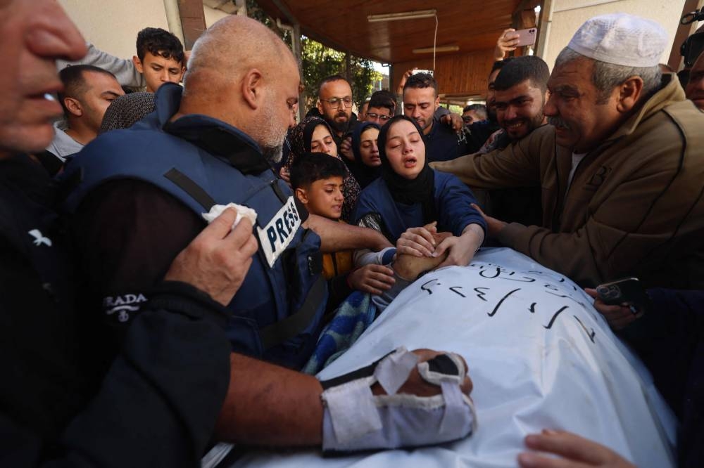 The wife (C) of Hamza Wael Dahdouh, a journalist with the Al Jazeera television network, and his father Al Jazeera's bureau chief in Gaza, Wael Al-Dahdouh (L) mourn over his body during his funeral, after he was killed in a reported Israeli air strike in Rafah in the Gaza Strip on Sunday. AFP