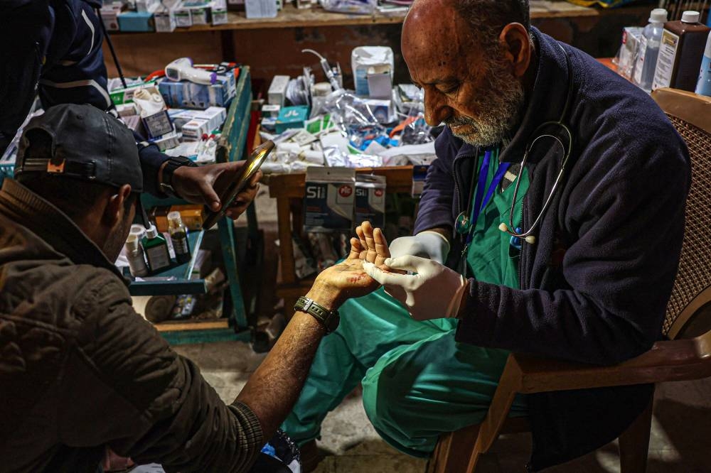 Zaki Shaheen, a retired nurse who turned his shop into a clinic to help displaced Gazans, treats a wounded man at his make-shift clinic in Rafah, on Wednesday. AFP