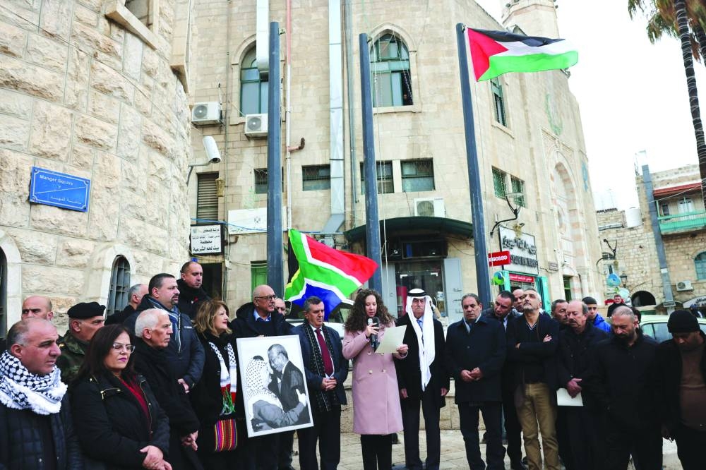 A Palestinian man holds a portrait of late Palestine Liberation Organisation (PLO) leader Yasser Arafat and South Africa's anti-apartheid icon Nelson Mandela before raising the South African  national flag outside the municipality building in Bethlehem in the occupied West Bank, yesterday.