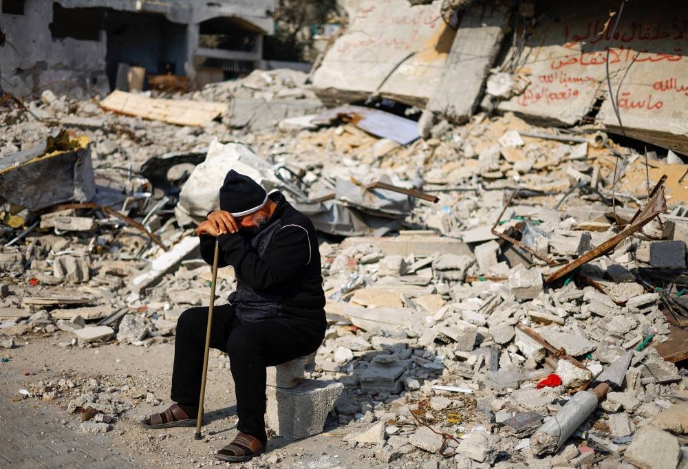Ziad Mansour, a neighbour of the Abu Aweidah family, sits next to writing painted on a wall amid the rubble of the family's house, which was destroyed in a deadly Israeli strike, in Rafah, Gaza Strip, January 9. REUTERS