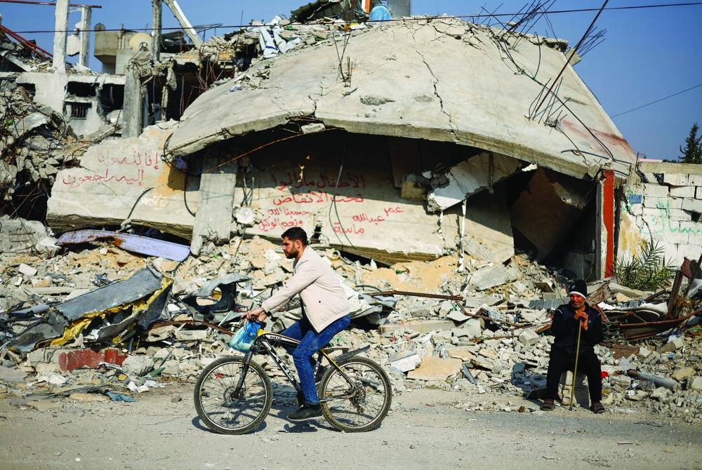 Ziad Mansour, a neighbour of the Abu Aweidah family, sits next to writing painted on a wall amid the rubble of the family’s house, which was destroyed in a deadly Israeli strike amid the ongoing conflict, in 
Rafah, Gaza Strip. The writing reads: “Children remaining under the 
rubble, Omar, Abdullah and Massa”.