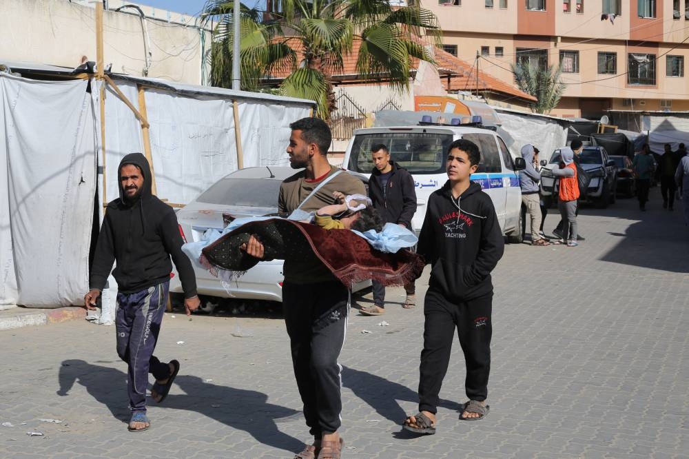 A man carries the body of a boy killed in an Israeli strike, as he walks to bury him at the Nasser hospital premises, as Palestinians cannot reach the cemetery due to the Israeli ground operation, in Khan Younis, on Monday. REUTERS