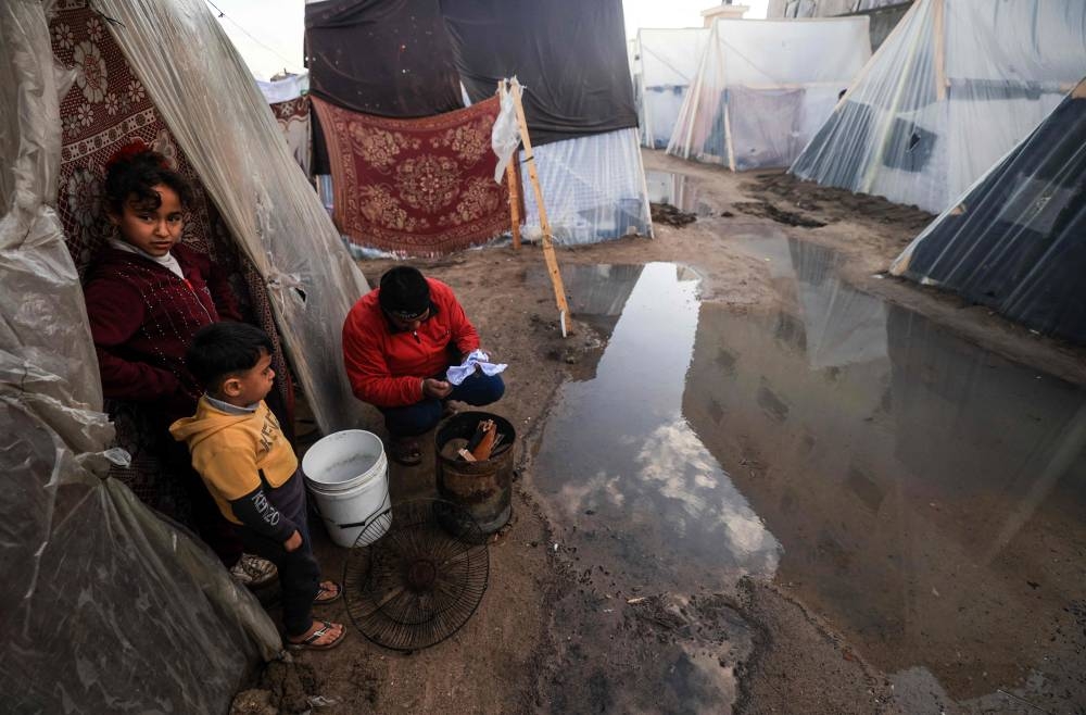 Children look on as a displaced Palestinian man lights a fire amid tents flooded by heavy rain, at a makeshift camp set up by people who fled the ongoing battles in Rafah in the southern Gaza Strip on Saturday. AFP