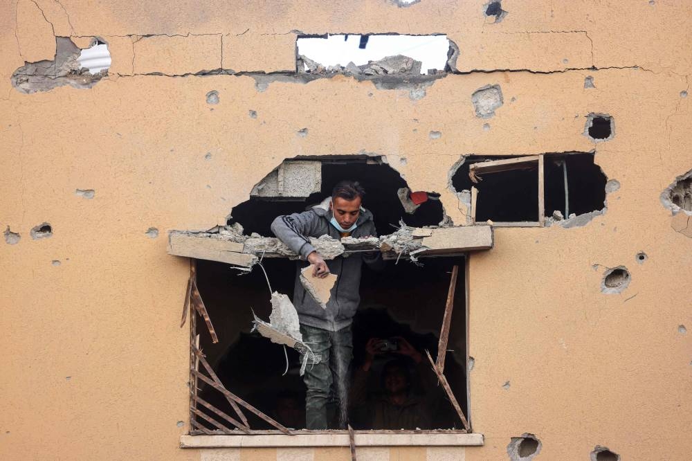 A man looks through the window of a building damaged by Israeli bombing, shows members of a family standing on a rooftop, in Rafah in the southern Gaza Strip on Saturday. AFP